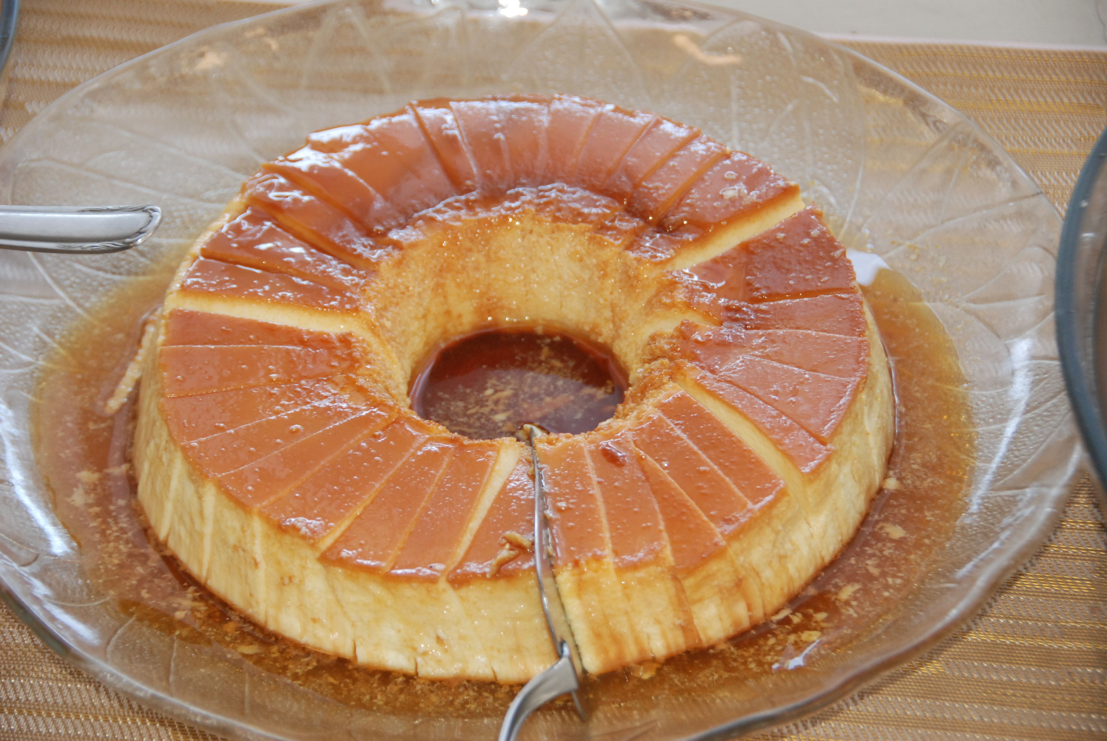 A caramel flan on a clear glass plate with a fork.