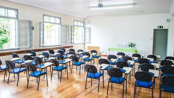 A classroom with rows of desks and chairs, large windows, and a white ceiling.
