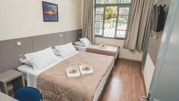 Habitación de hotel con dos camas, un escritorio, una silla, un ventanal con cortinas y un cuadro en la pared.