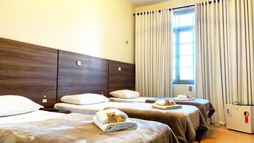 A hotel room with three beds, a ceiling fan, a window with curtains, and a minibar.