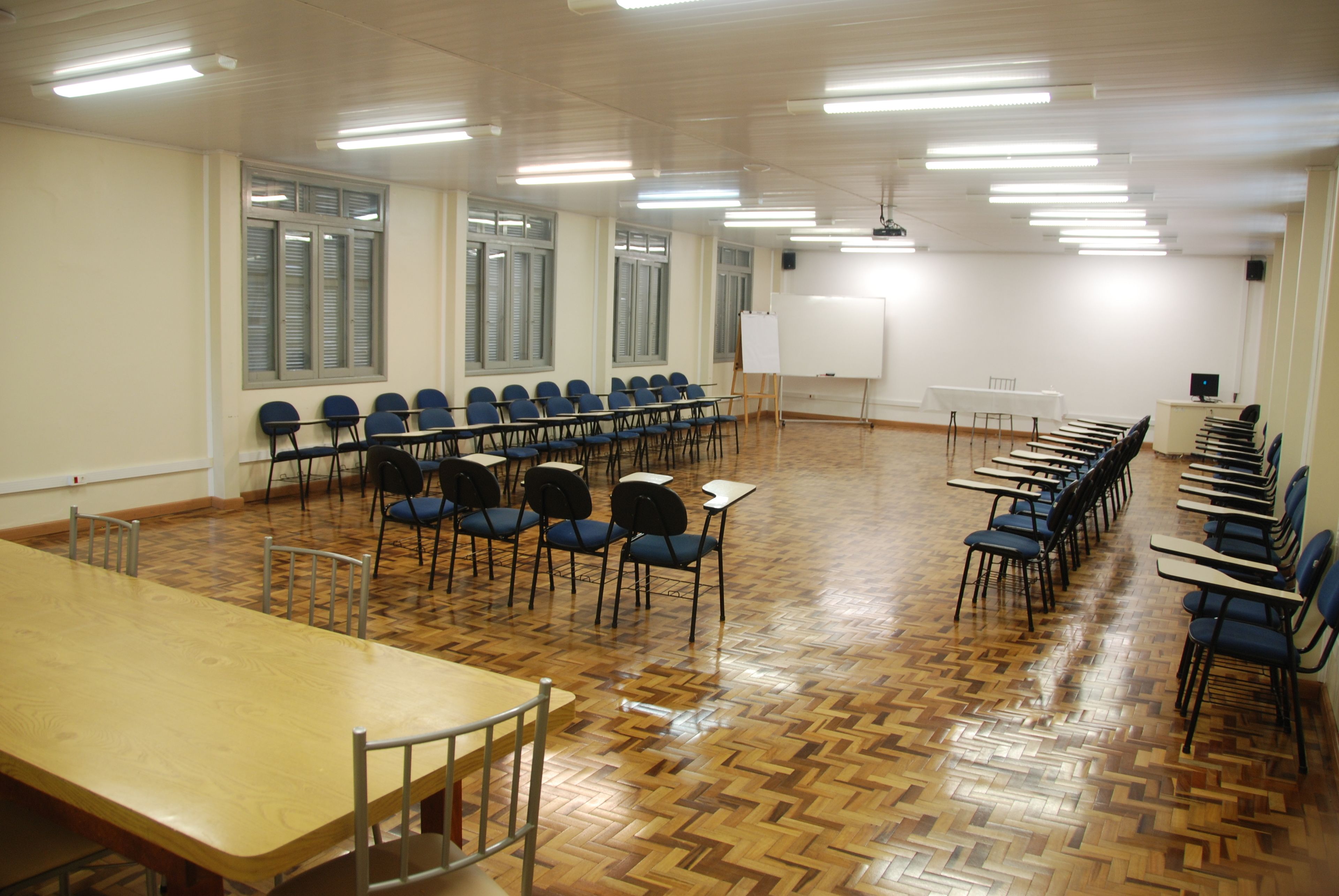 Una sala de conferències amb una taula llarga, files de cadires, una pissarra i una pantalla de projector.