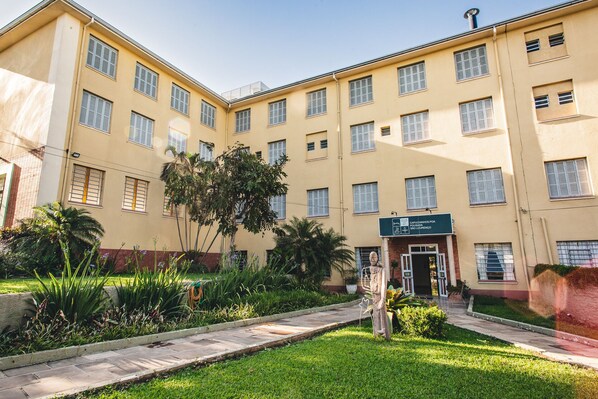 A multi-story building with a central entrance, surrounded by a well-maintained garden with various plants and a paved pathway. - Hotel Pousada São Lourenço (Porto Alegre)