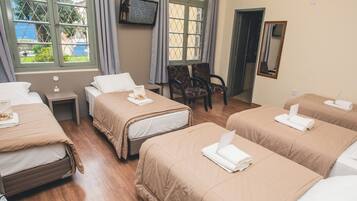 A hotel room with four beds, a television on the wall, a chair, and a mirror.