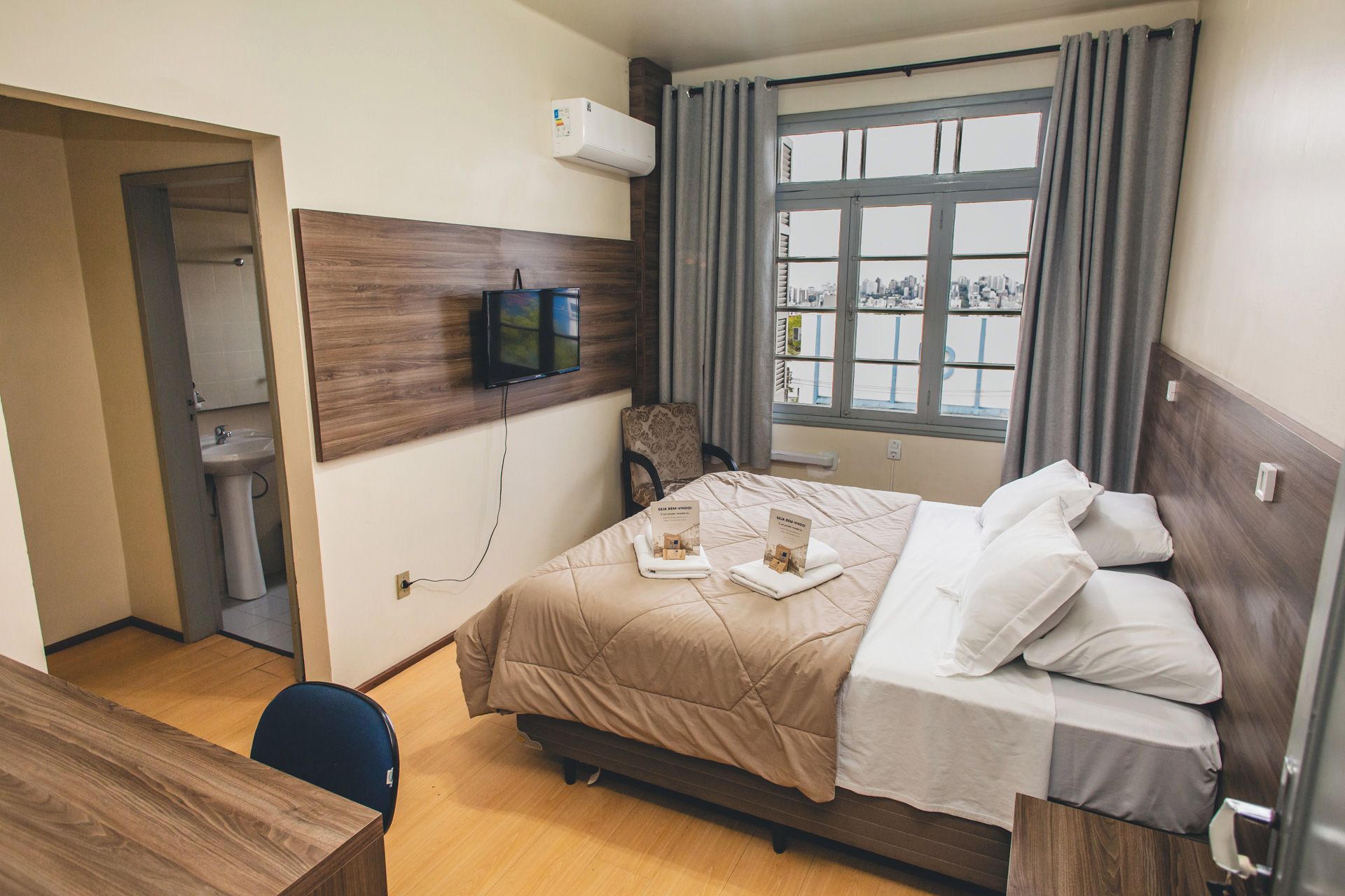 A hotel room with a bed, a desk, a chair, a TV, and a window with curtains.