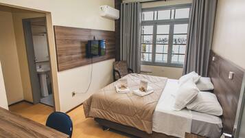 A hotel room with a bed, a desk, a chair, a TV, and a window with curtains.