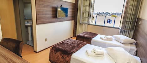 A hotel room with two beds, a desk, and a view of the city through a window.