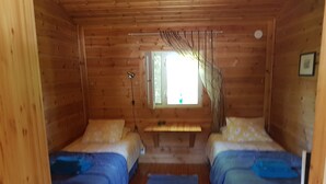 A cabin with two beds, a window with blinds, a wooden ceiling, and a small bench. - Miekkala Majoitus (Lappeenranta)
