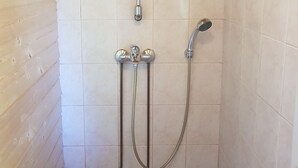 A shower area with a vertical showerhead, a handheld showerhead, and a wall-mounted faucet. - Miekkala Majoitus (Lappeenranta)