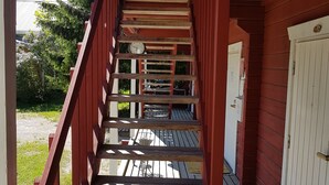A wooden staircase leading to a covered area with a white door and a clock on the wall. - Miekkala Majoitus (Lappeenranta)