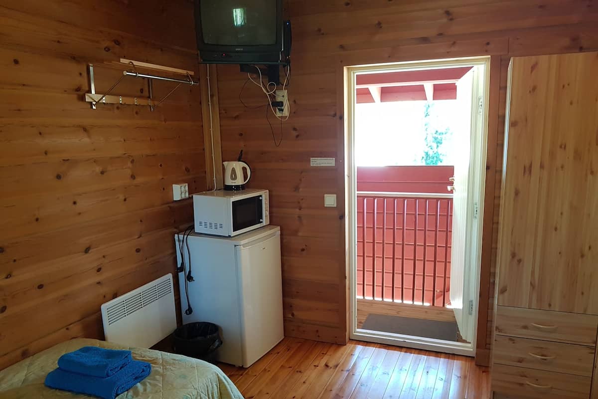 A compact room with a bed, a small refrigerator, a microwave, a television, and a door leading to an outdoor area.