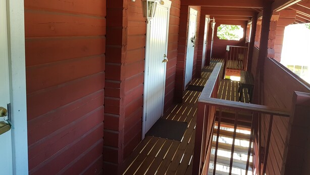 A corridor with wooden walls and a metal railing, leading to a door with a light fixture above it. - Miekkala Majoitus (Lappeenranta)