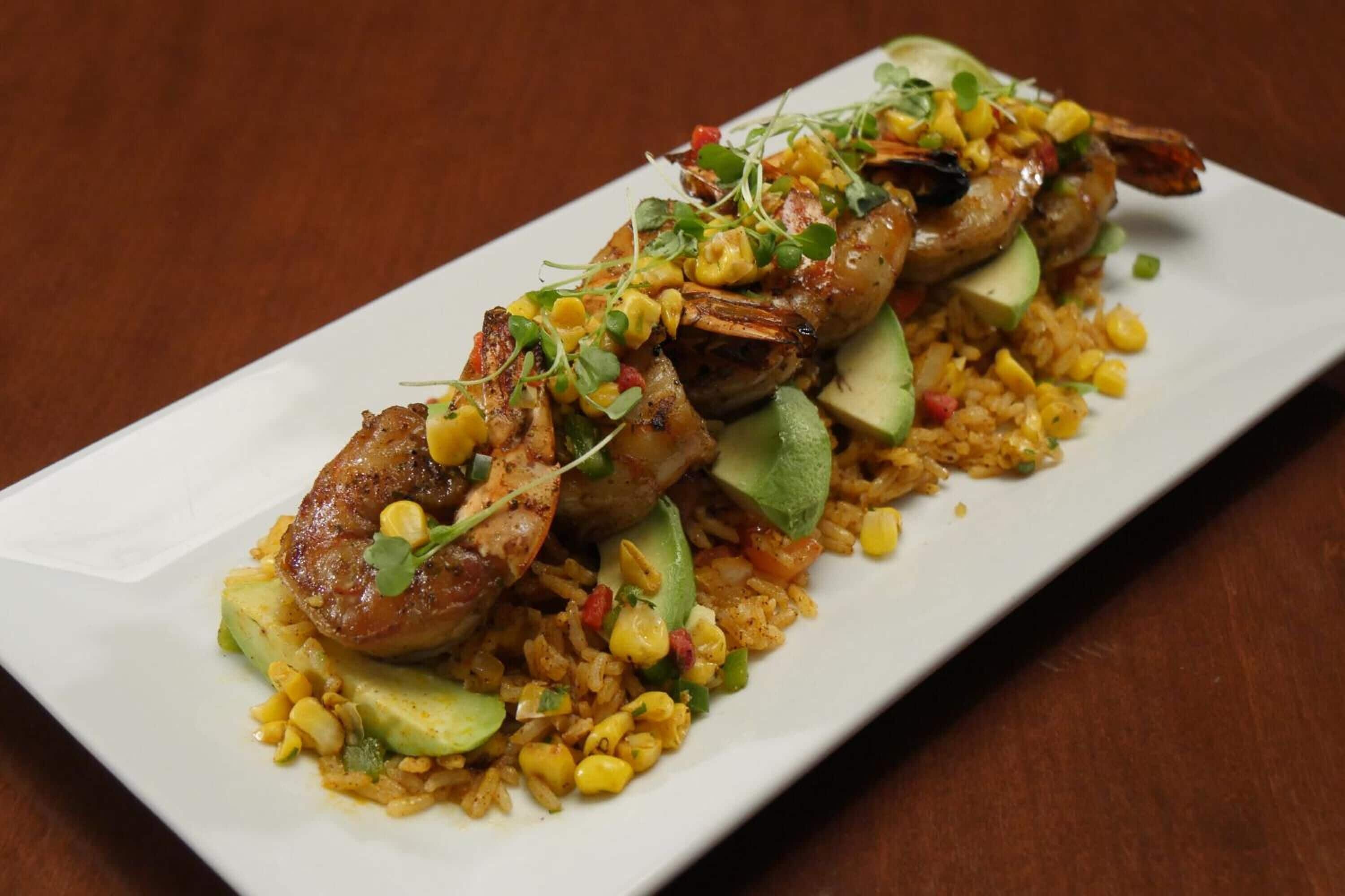 Un plato con carne a la parrilla, aguacate, maíz y arroz.