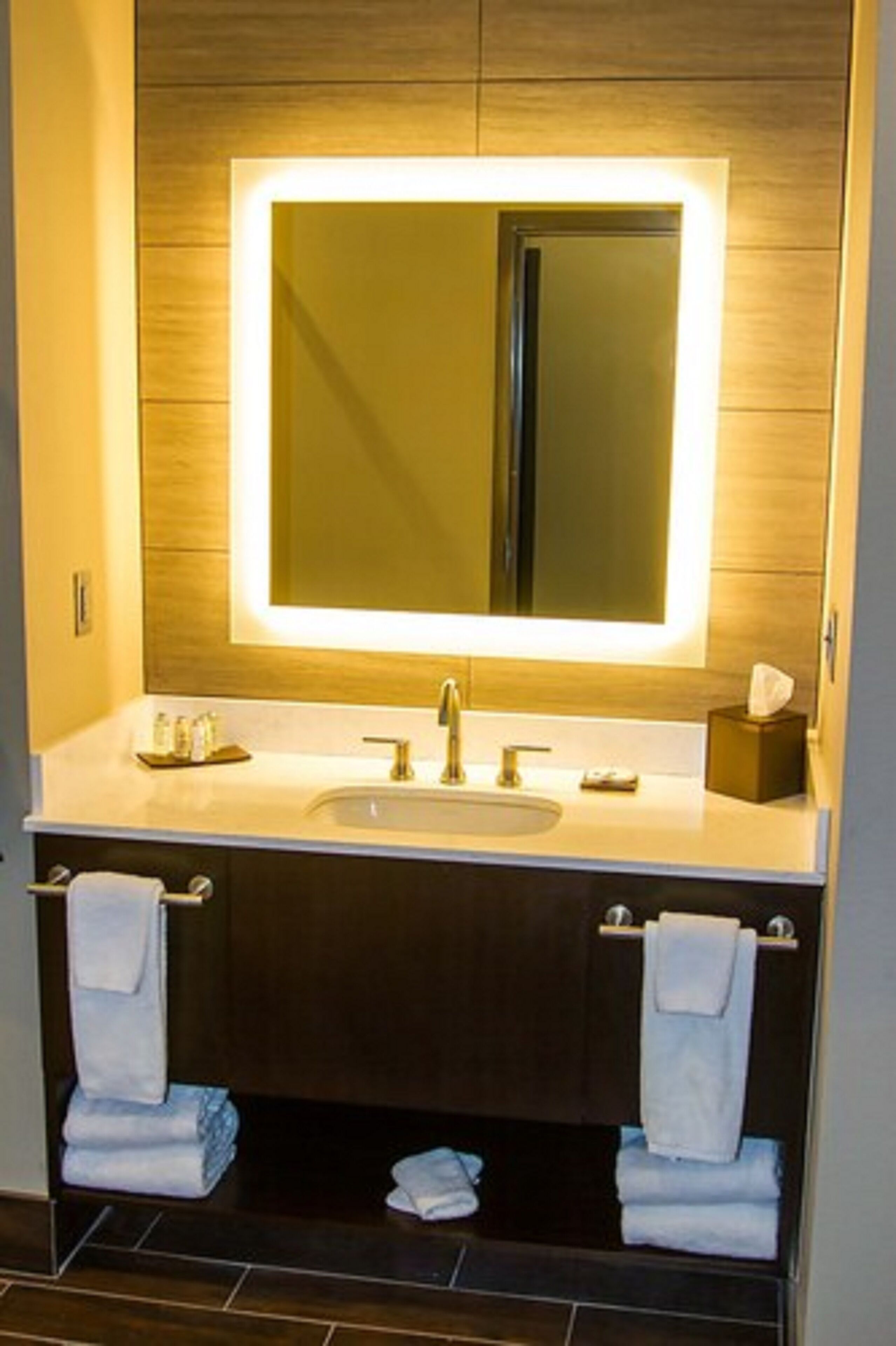 Un baño moderno con un espejo grande, un lavamanos y dos barras para toallas.