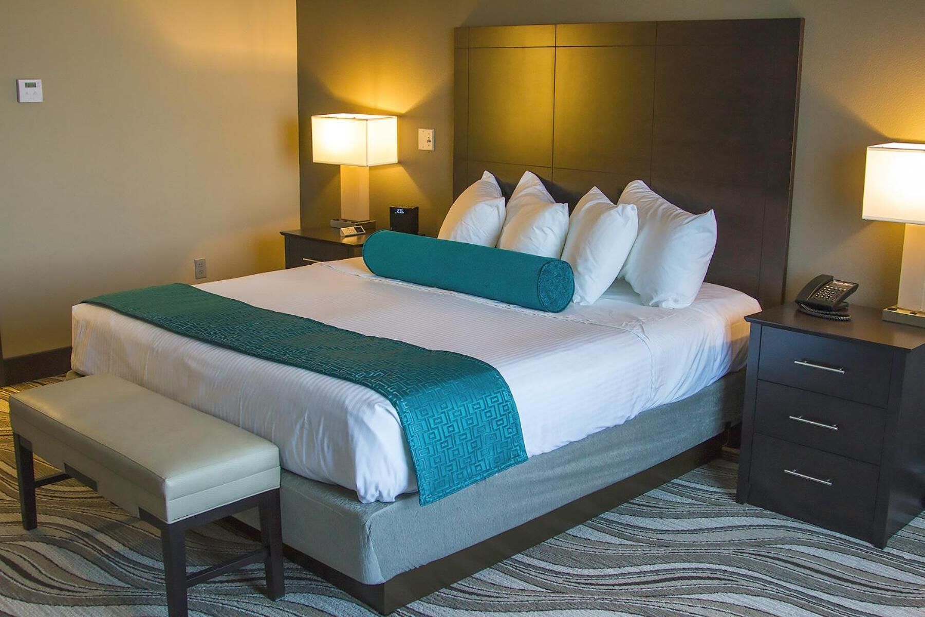A hotel room with a bed, bedside tables, a bench, and a wall-mounted lamp.