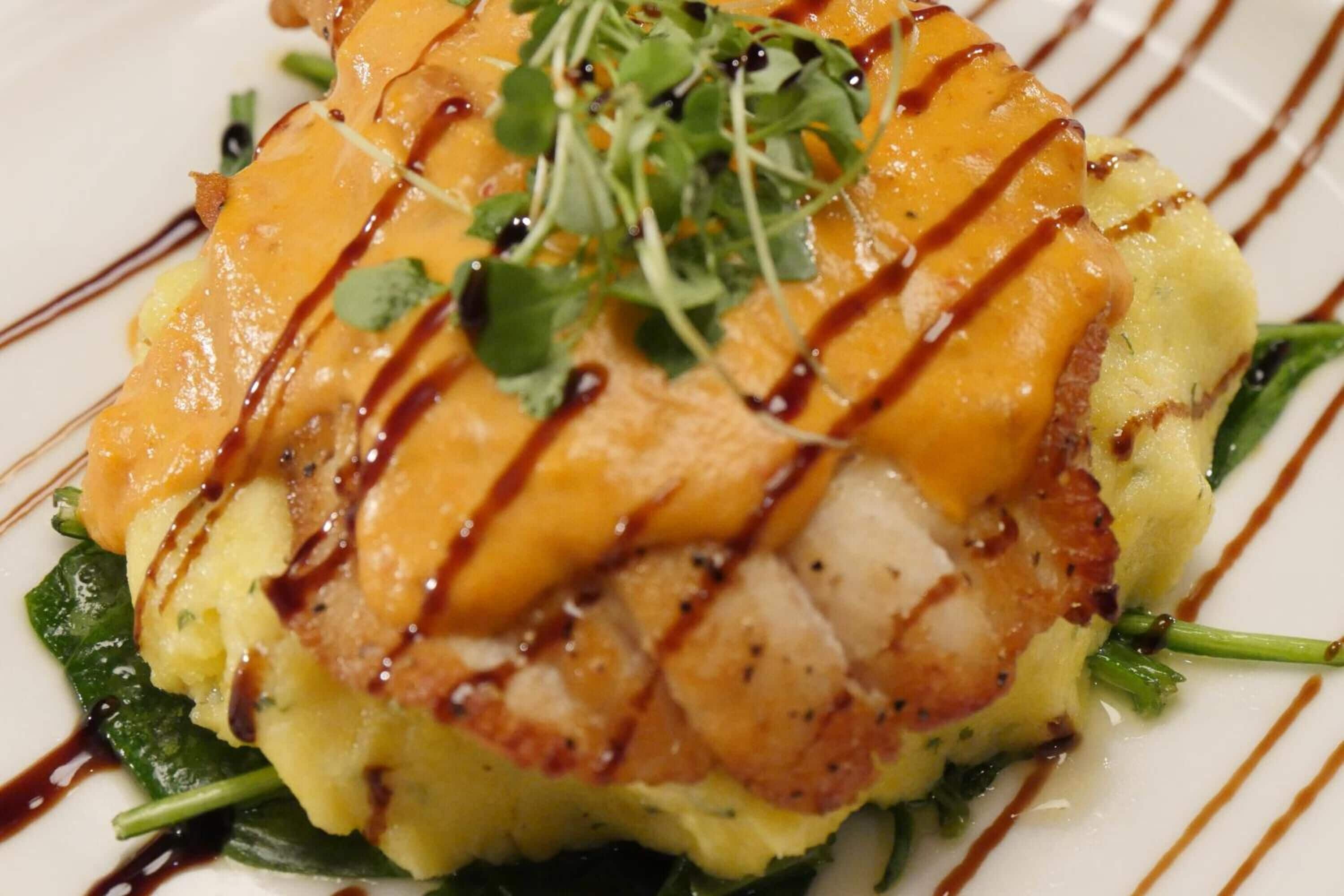 A dish with grilled fish, mashed potatoes, and greens, drizzled with sauce.