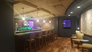 A bar area with a long counter, multiple stools, and a television screen. - River Bend Casino & Hotel (Wyandotte)