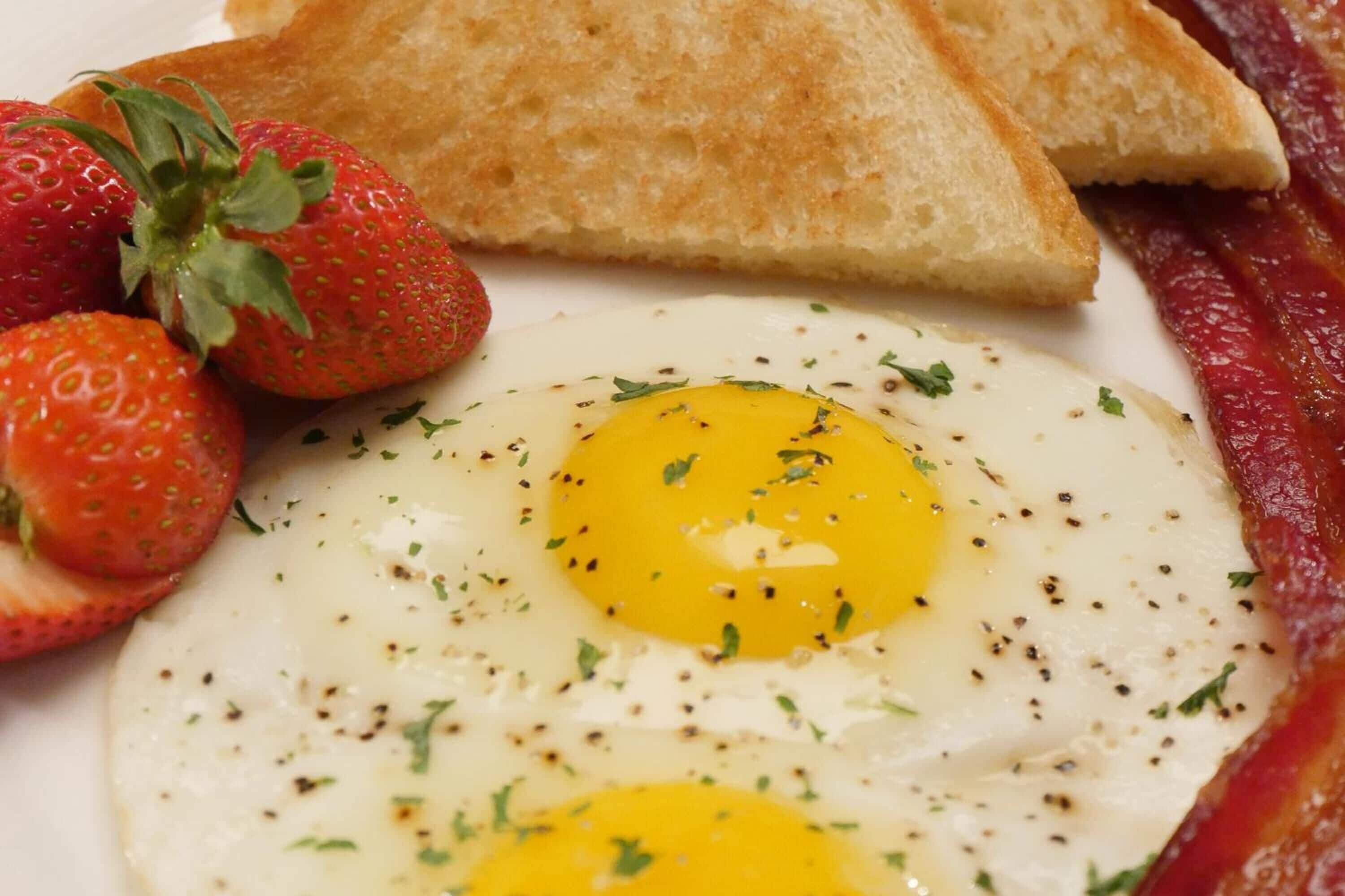 A breakfast plate with eggs, toast, strawberries, and bacon.