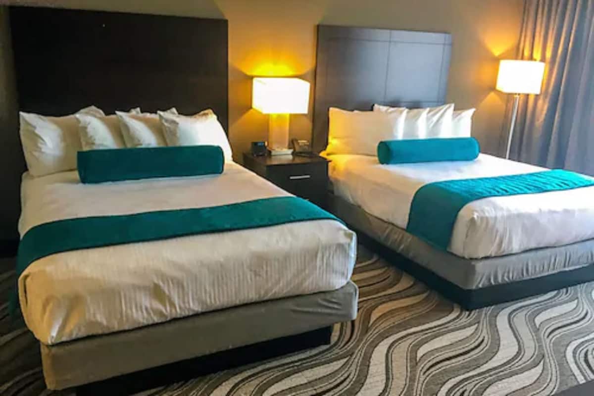 A hotel room with two beds, each with white bedding and teal accents, a dark headboard, and a patterned carpet.