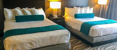 Une chambre d’hôtel avec deux lits, chacun agrémenté de draps blancs et de touches de couleur turquoise, d’une tête de lit sombre et d’un tapis à motifs.