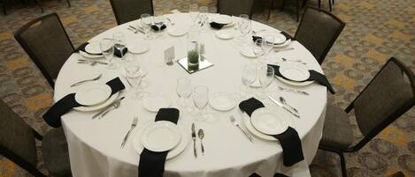 A round dining table set for eight with white tablecloths, black napkins, and silverware.
