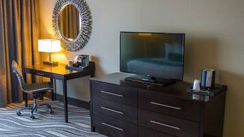 Hotelkamer met een flatscreen televisie op een dressoir, een bureau met een lamp, een stoel en een grote spiegel aan de muur.