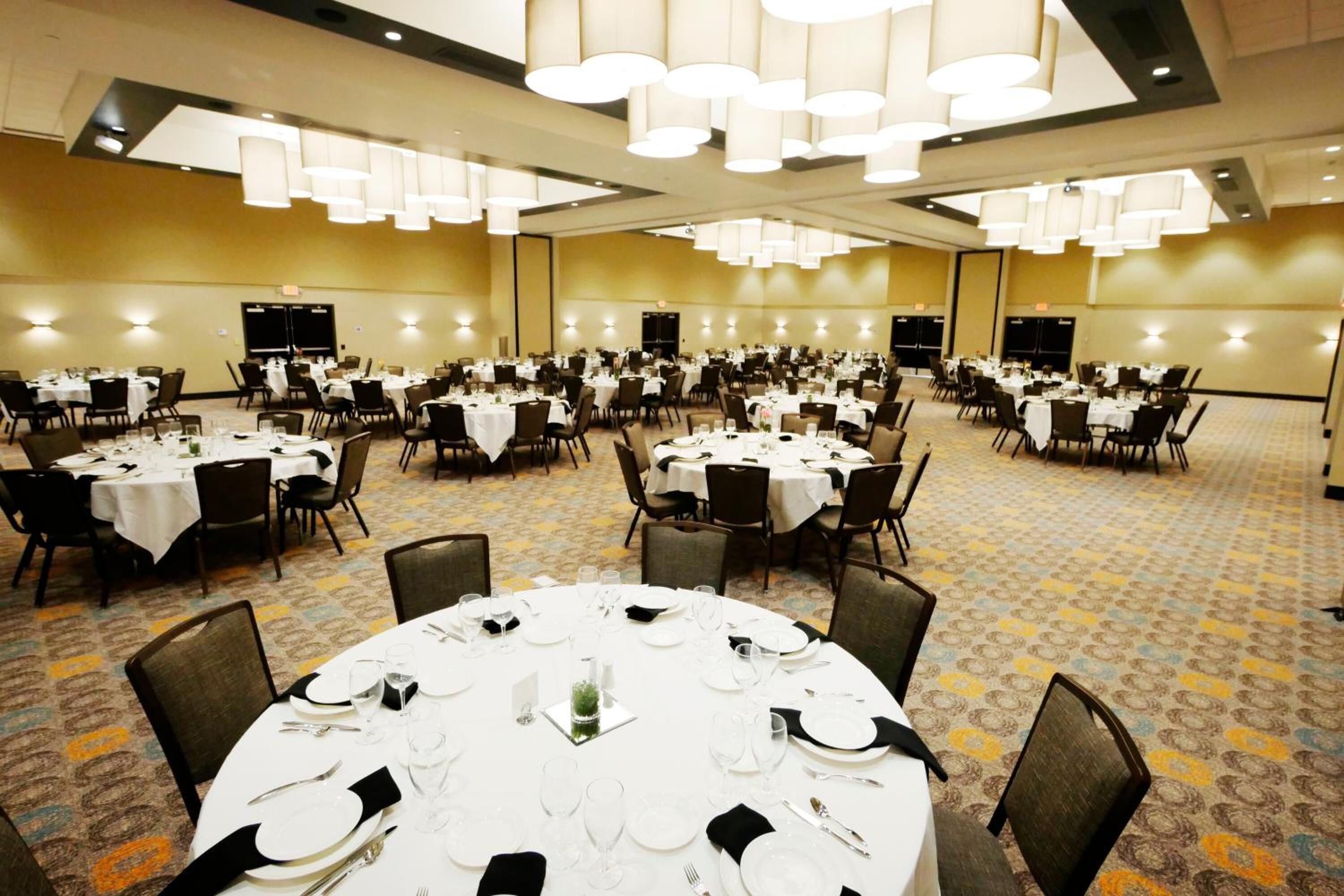 Un amplio salón de banquetes con mesas redondas dispuestas para el servicio de comidas, equipado con sillas y vajilla.