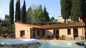 Una casa con piscina rodeada de rocas, un patio con sillas y un jardín con árboles y plantas.