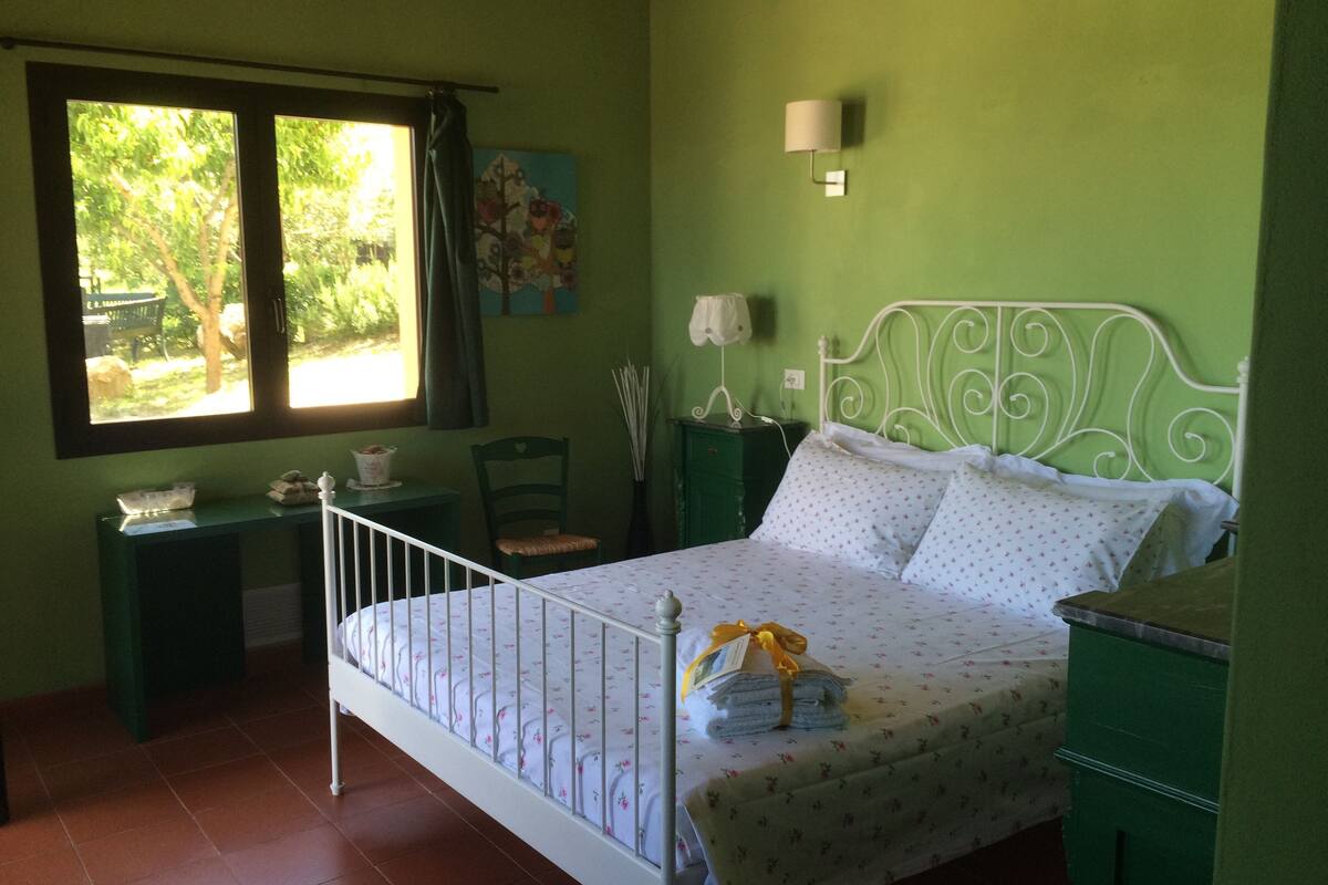 A bedroom with a bed, green walls, a window, a desk, and a chair.