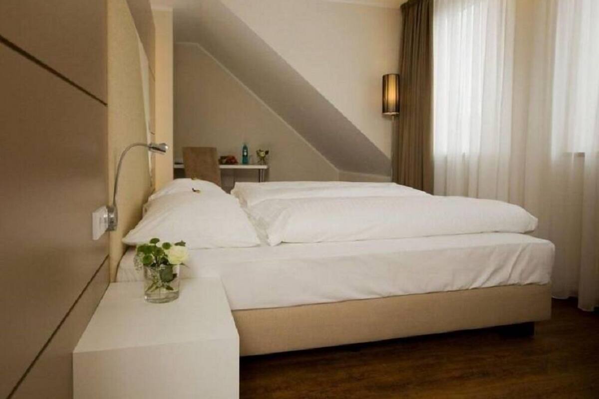 Une chambre d’hôtel avec un grand lit, une table de chevet, une lampe et une vue sur l’extérieur à travers des rideaux transparents.