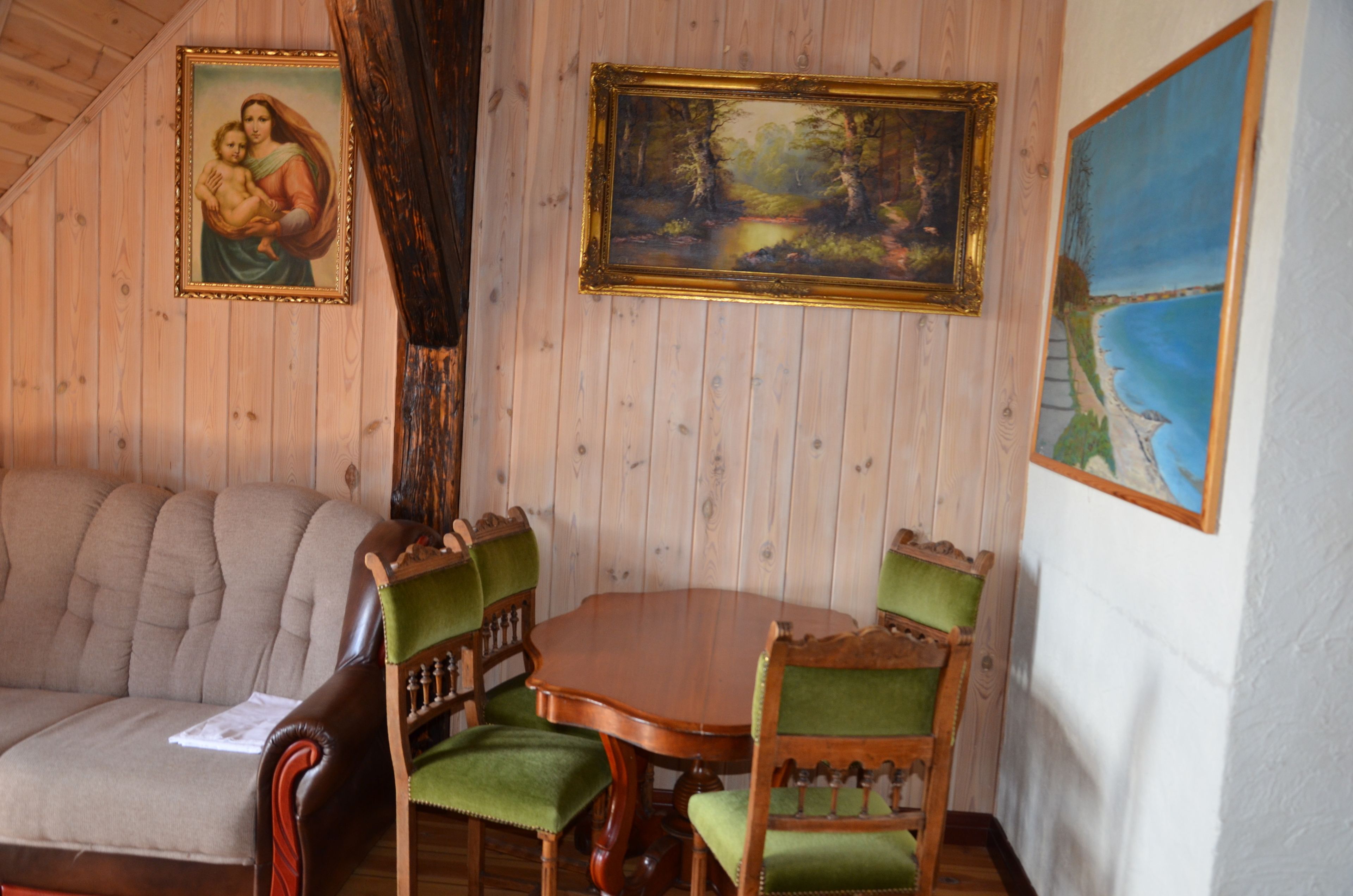 Une pièce aux murs lambrés, comprenant une table à manger et des chaises, un canapé et trois tableaux encadrés.