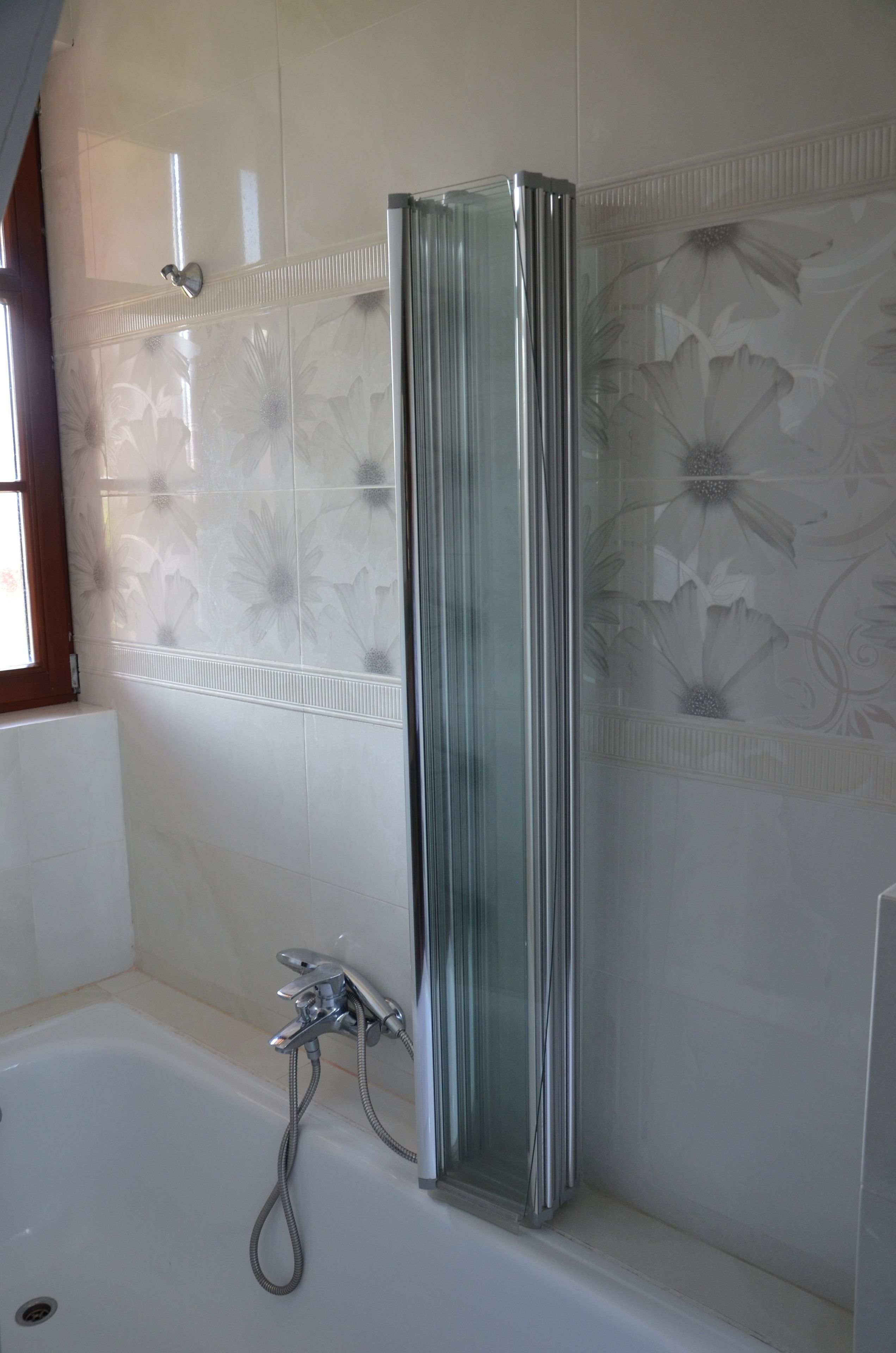 Un baño con cabina de ducha de vidrio, bañera y azulejos decorativos con motivos florales.