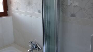 Un baño con cabina de ducha de vidrio, bañera y azulejos decorativos con motivos florales.