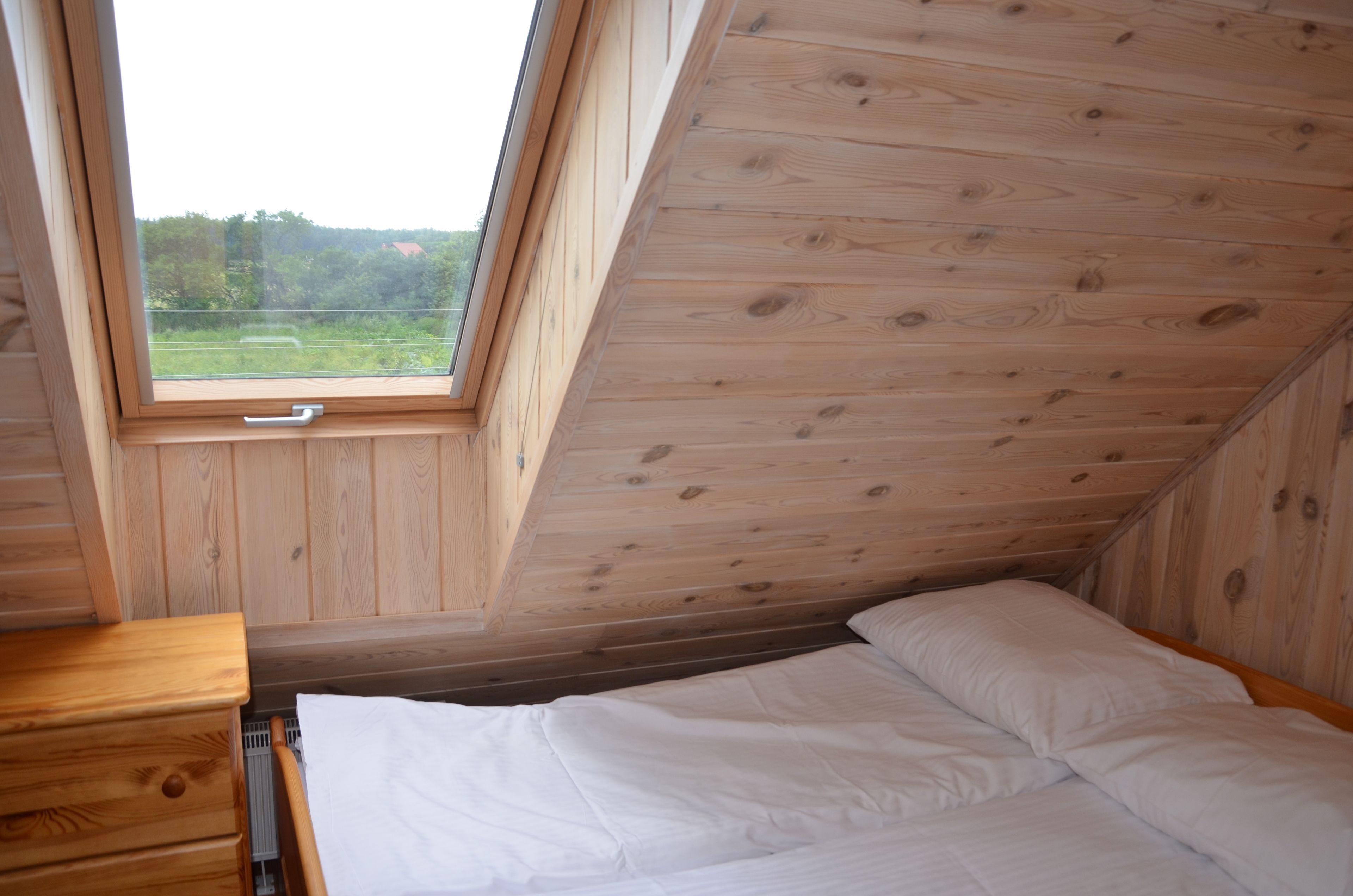 Un dormitorio con techo de madera y tragaluz, una cama con ropa de cama blanca y un aparador de madera.