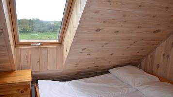 Un dormitorio con techo de madera y tragaluz, una cama con ropa de cama blanca y un aparador de madera.