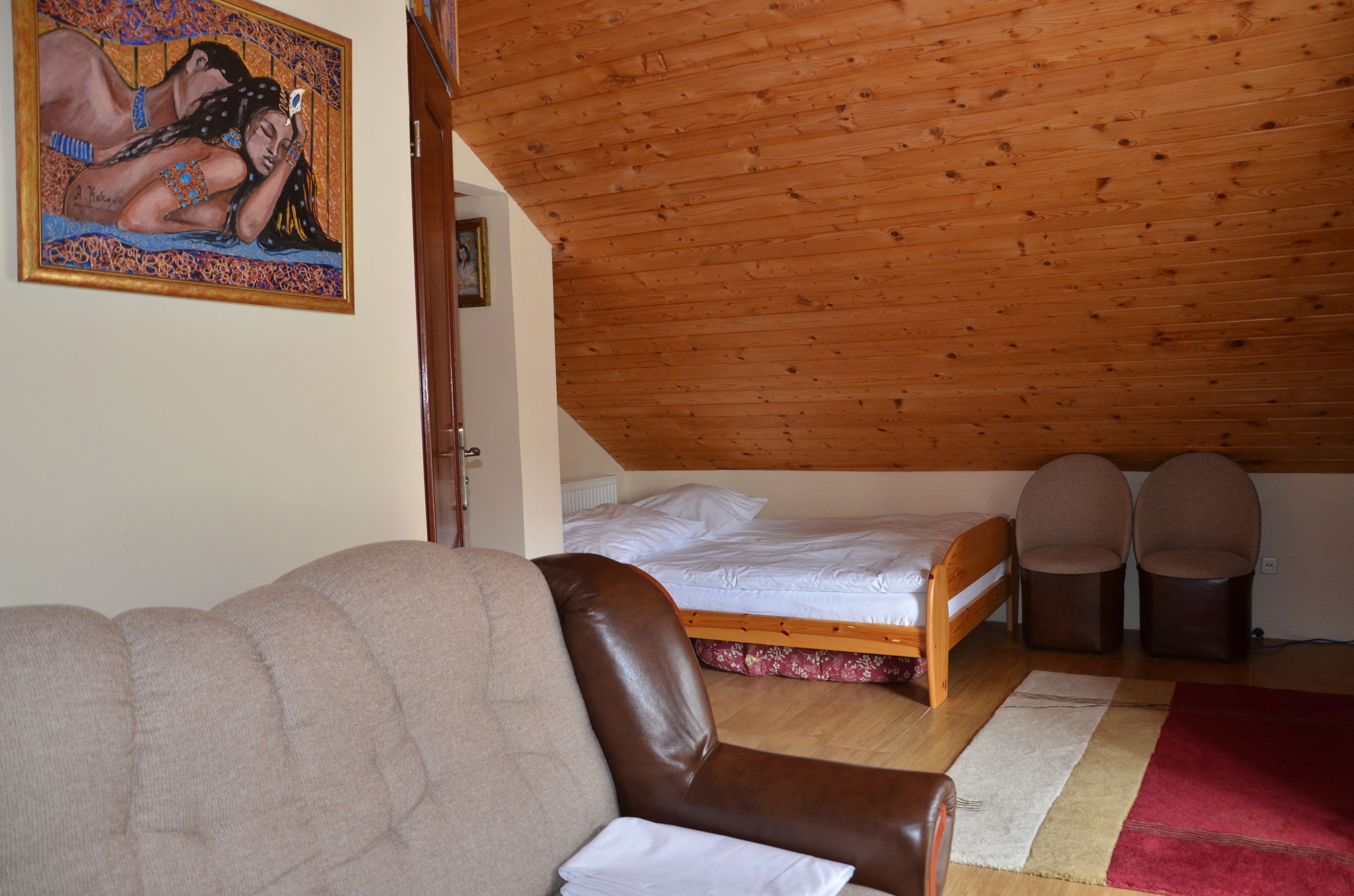 A bedroom with a wooden ceiling, a bed, a sofa, and a painting on the wall.