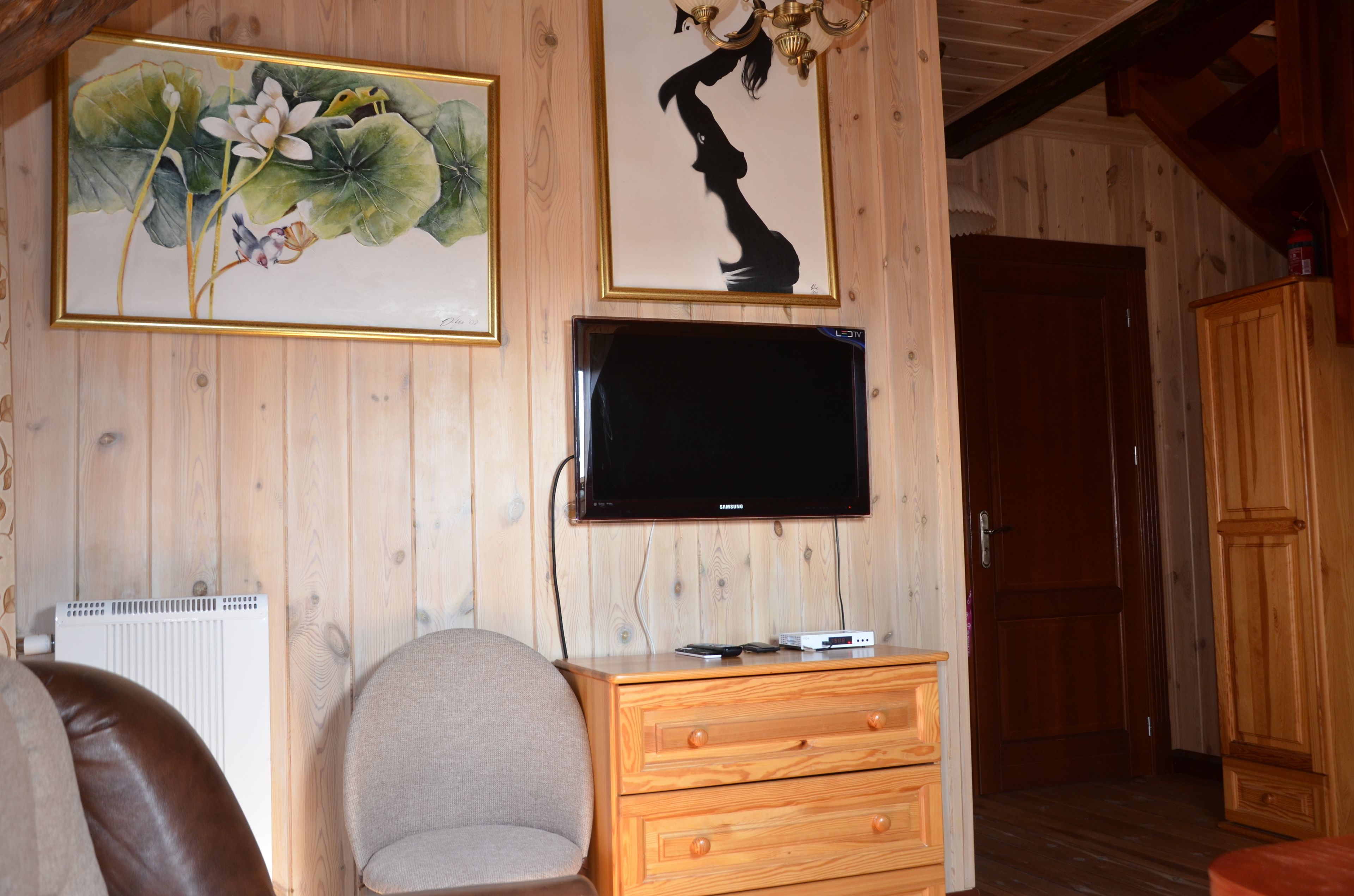 A wooden-paneled room with a flat-screen TV mounted on the wall, a wooden cabinet, and a chair.