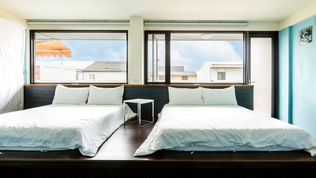 A hotel room with two single beds, a small table, and large windows offering a view of the cityscape.