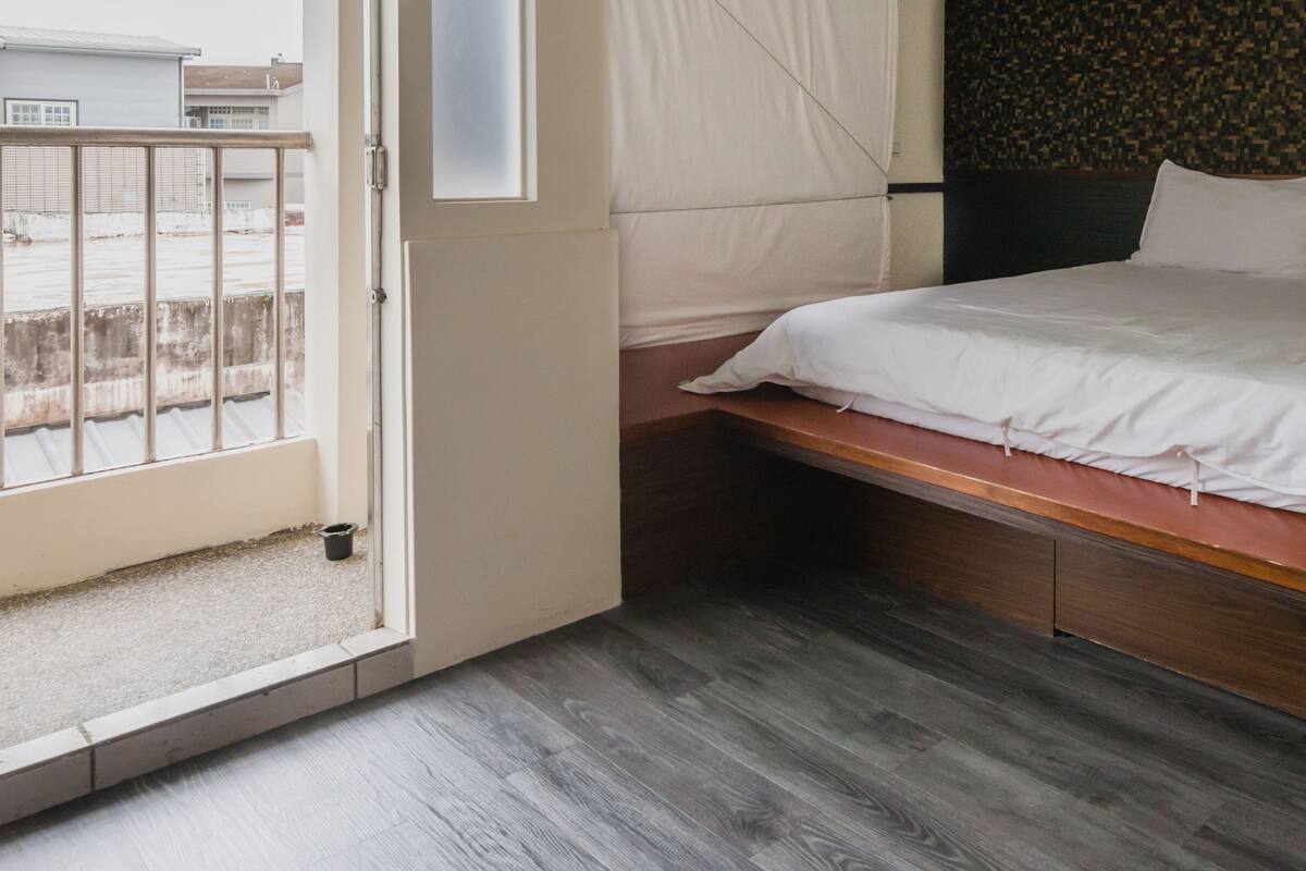 A bedroom with a bed, a wooden bench, a small window, and a view of the outside.