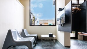 A modern room with a large window, two grey chairs, a small round table with a tissue box, and a TV mounted on the wall.