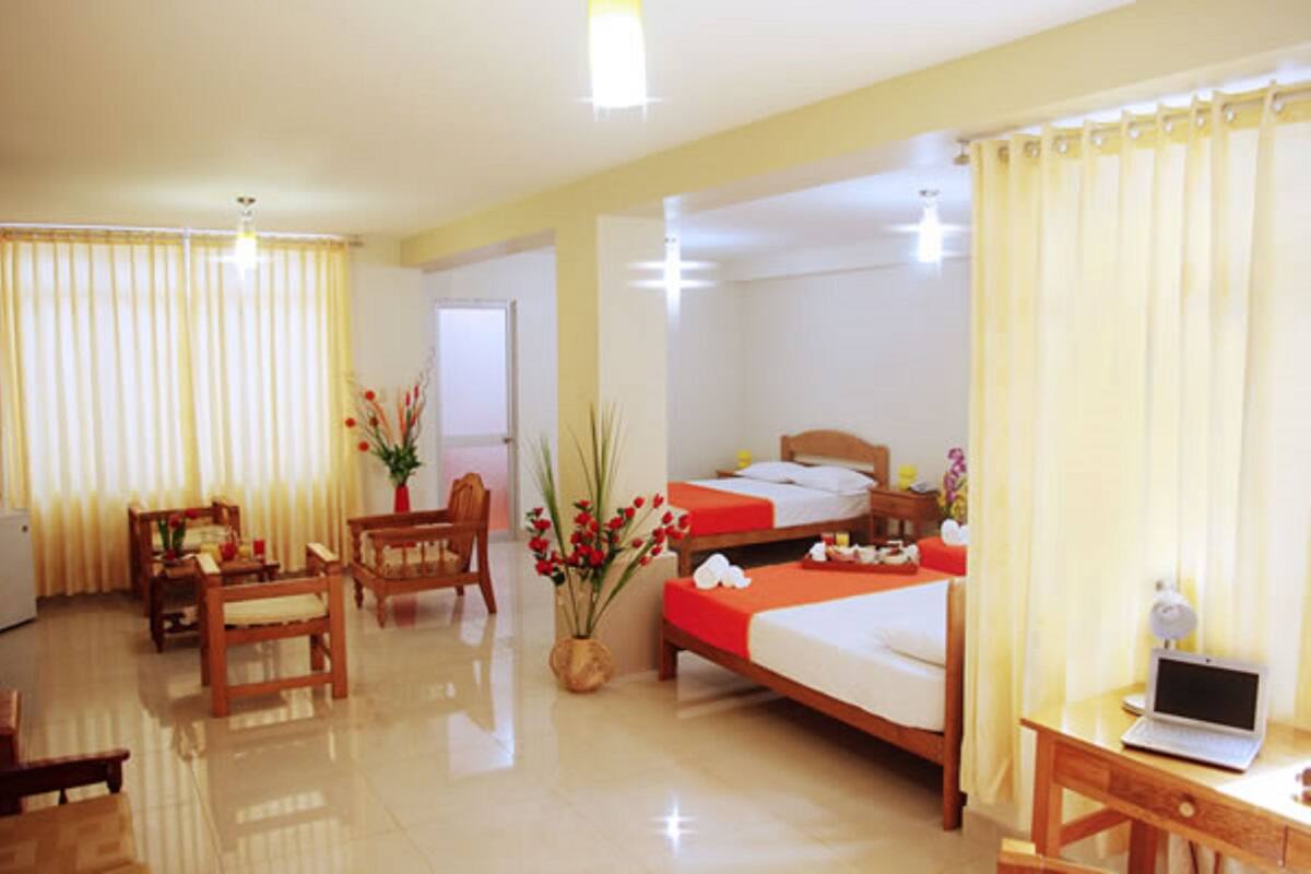 A hotel room with two beds, a desk with a laptop, a chair, a small table, and a potted plant.