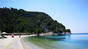 Una playa con agua cristalina, una orilla arenosa y una colina boscosa al fondo.