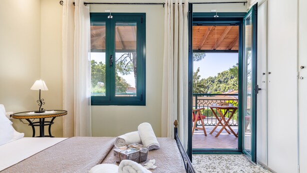 Habitación de hotel con cama, una mesa con lámpara, ventana con cortinas y vistas al balcón exterior.