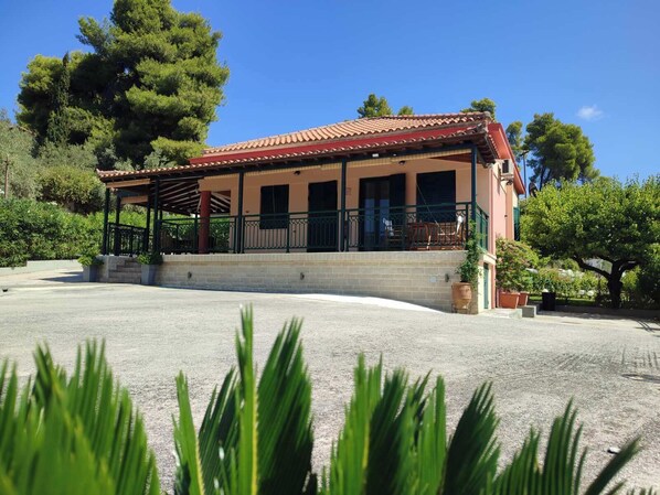 A two-story building with a red-tiled roof, a covered porch with a railing, and a paved driveway.