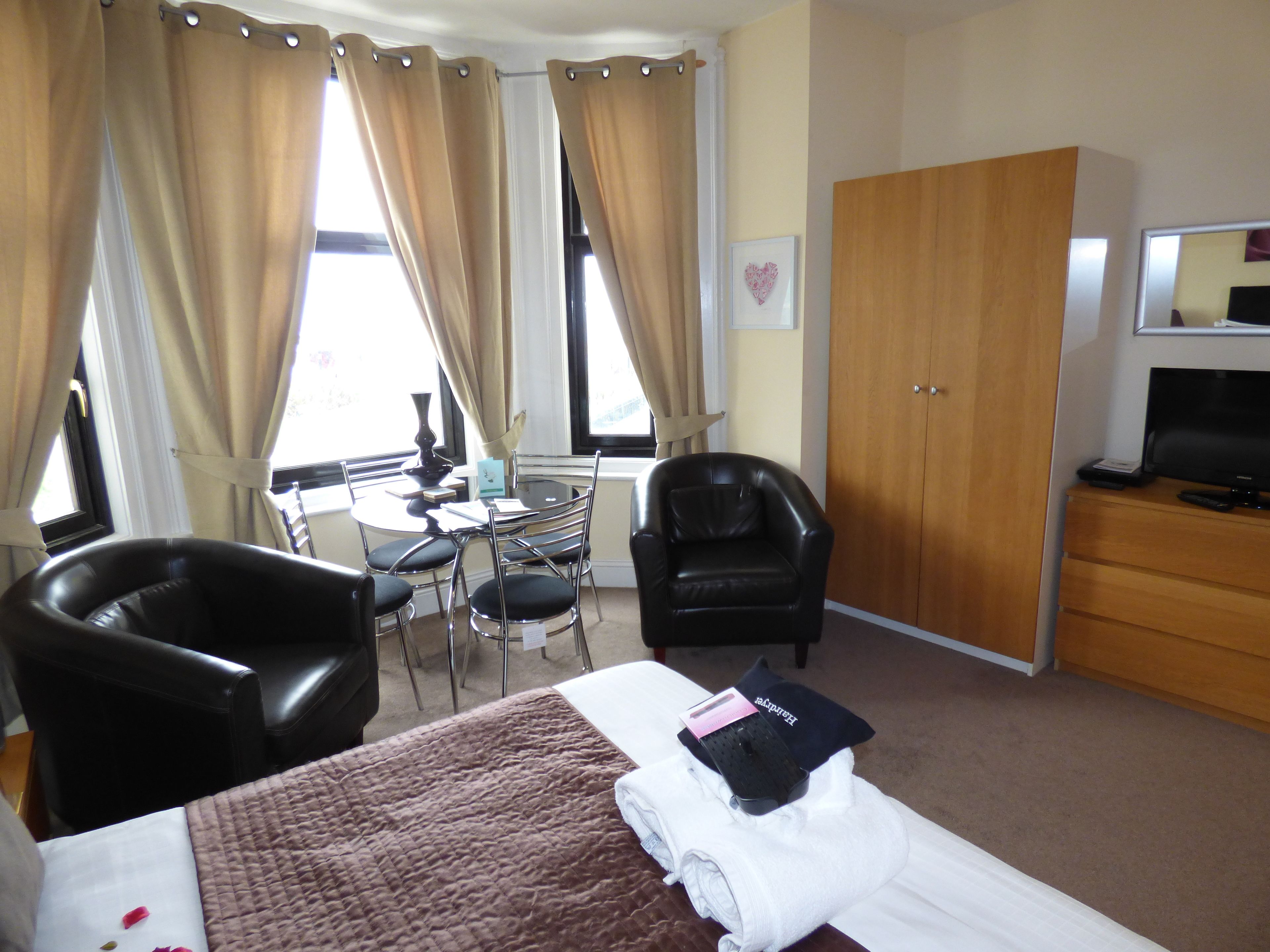 A hotel room with a bed, a desk, a chair, a wardrobe, and a television.