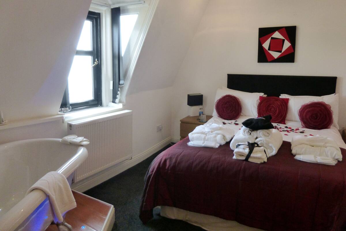 Une chambre d’hôtel avec un lit, une table de chevet, une lampe, une fenêtre et un radiateur.