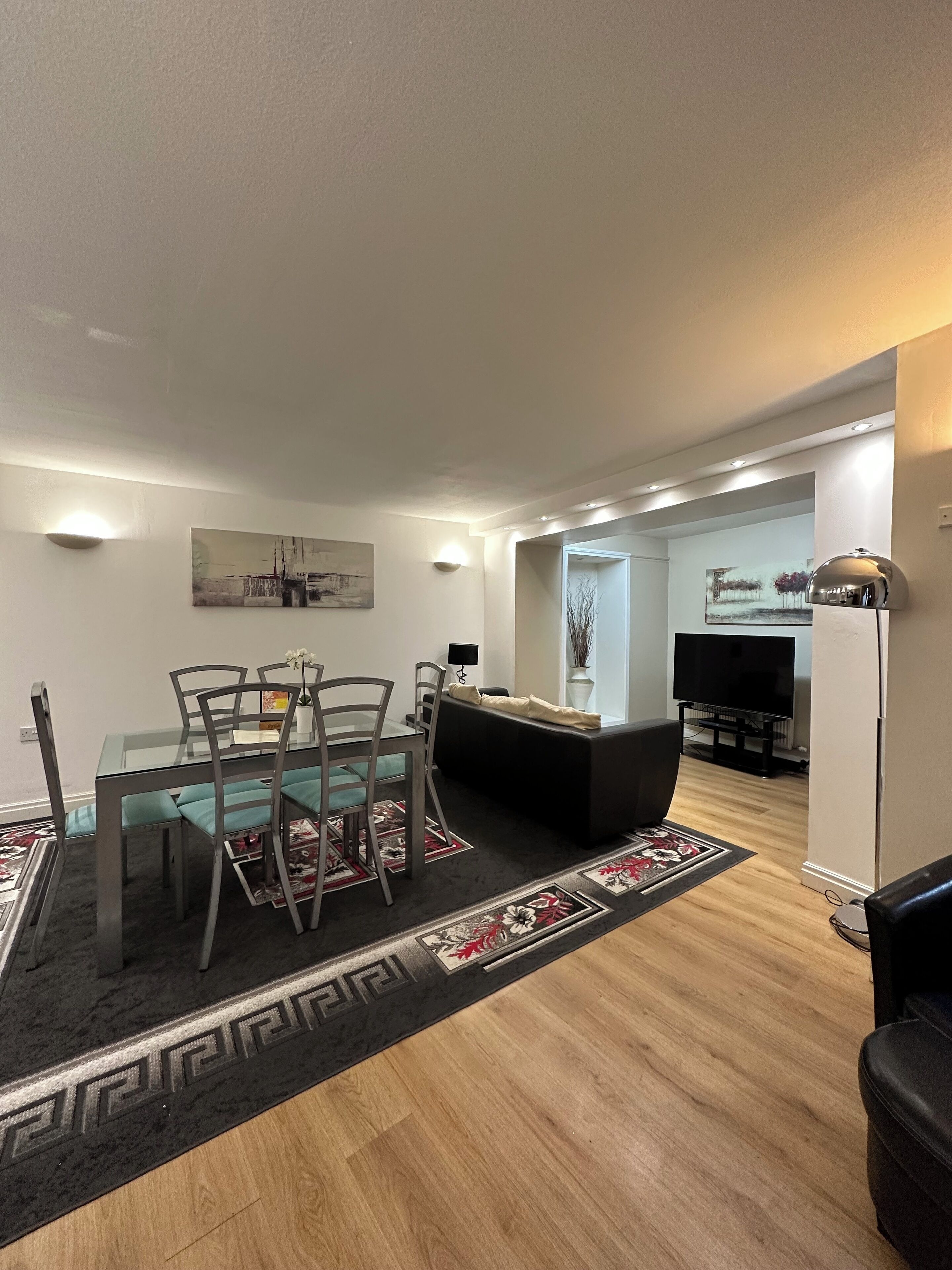 A modern living room with a dining area, a black sofa, a TV, and a fireplace.