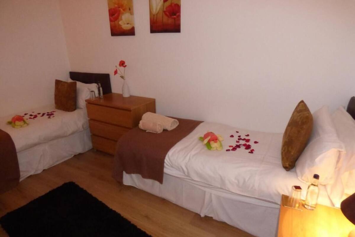 Une chambre avec deux lits simples, une commode, une table de chevet avec une lampe et des œuvres d’art accrochées au mur.