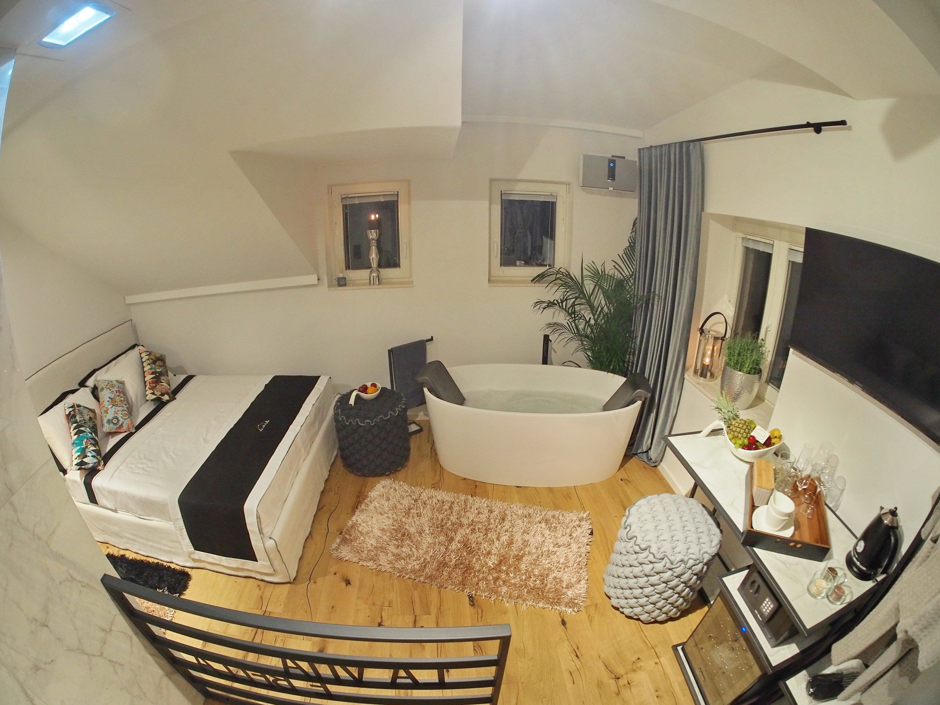 Een slaapkamer met een bed, een badkuip, een klein tafeltje met een plant en een raam.