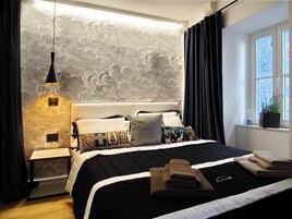Quarto moderno com uma cama grande, mesa de cabeceira, luminária pendente e janela com cortinas.