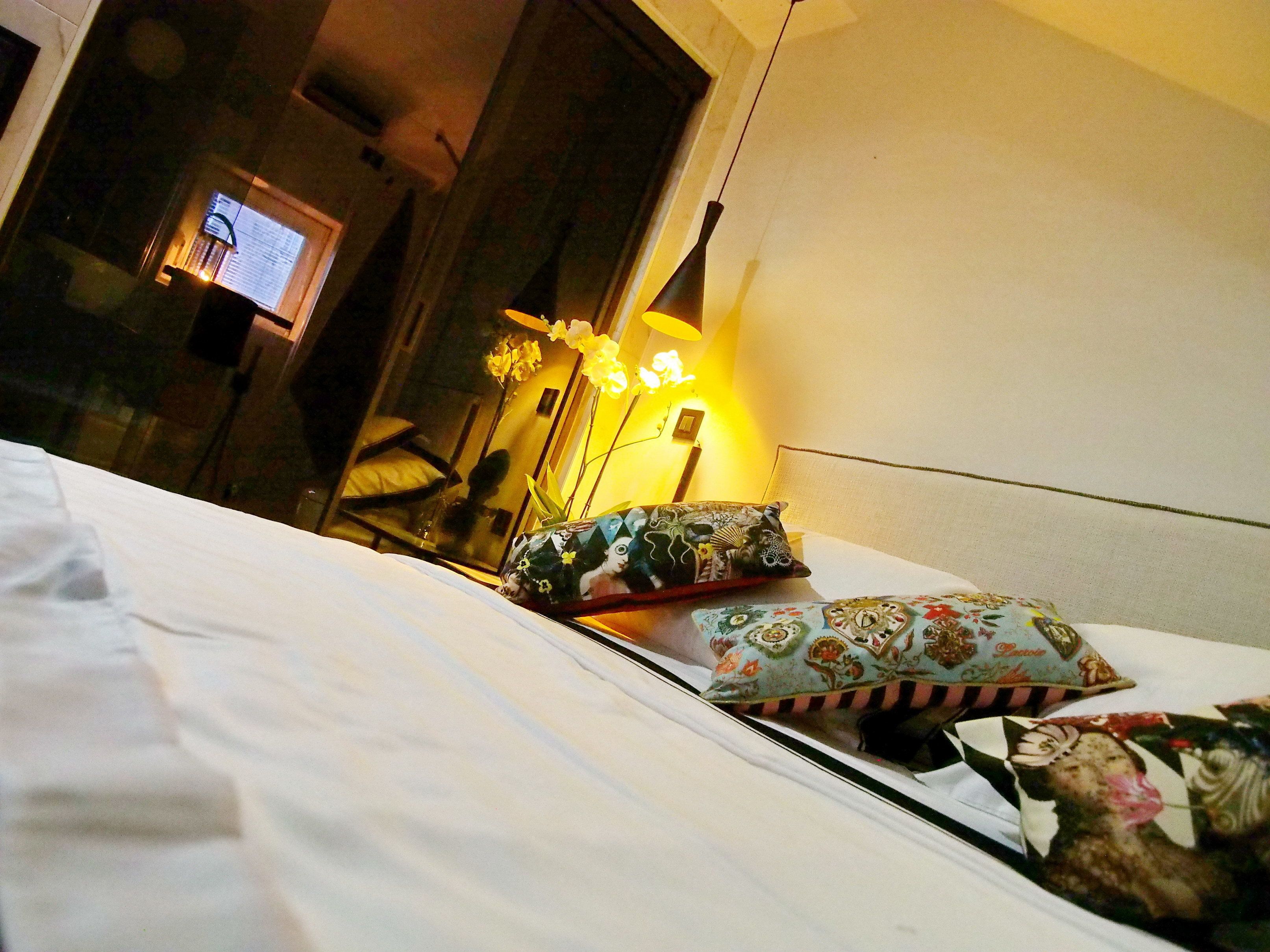 Une chambre d’hôtel avec un lit, des oreillers, un vase de fleurs et une lampe.